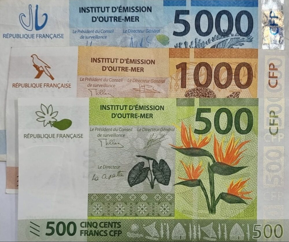 Three CFP franc banknotes in 5000, 1000, and 500 denominations arranged in a vertical stack, each featuring colourful illustrations. Three CFP franc banknotes in 5000, 1000, and 500 denominations arranged in a vertical stack, each featuring colourful illustrations.