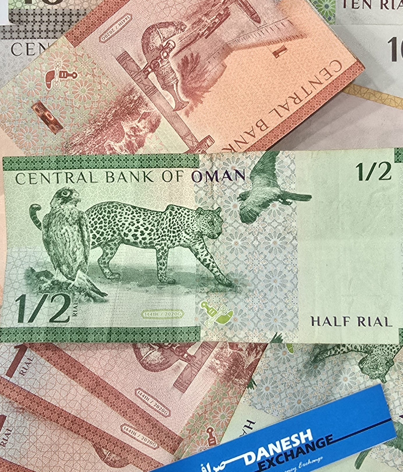 Omani banknotes including half‑rial and ten‑rial notes arranged together, featuring wildlife and traditional dagger designs above a blue Danesh Exchange label. Omani banknotes including half‑rial and ten‑rial notes arranged together, featuring wildlife and traditional dagger designs above a blue Danesh Exchange label.