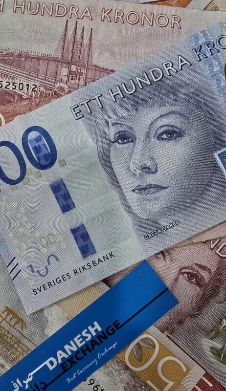 A mix of international banknotes, including a prominent Swedish 100‑kronor note featuring Greta Garbo, alongside 200‑ and 500‑kronor notes and other currencies in the background, with a blue Danesh Exchange label visible. A mix of international banknotes, including a prominent Swedish 100‑kronor note featuring Greta Garbo, alongside 200‑ and 500‑kronor notes and other currencies in the background, with a blue Danesh Exchange label visible.